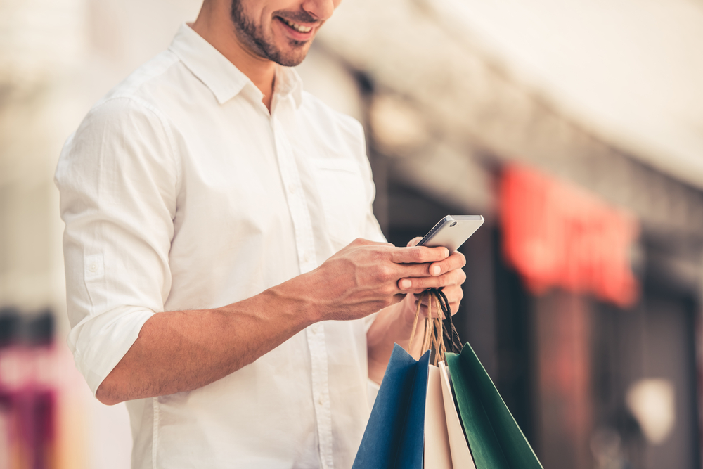 Guy,With,Shopping,Bags,Is,Using,A,Mobile,Phone